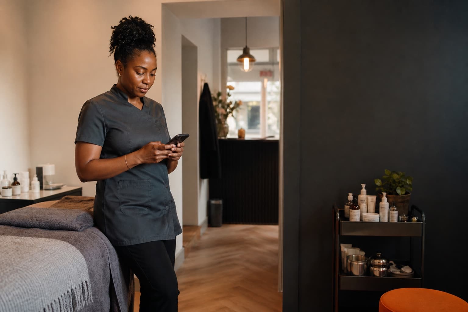 Illustrative editorial scene of a UK clinic owner checking her phone between appointments.
